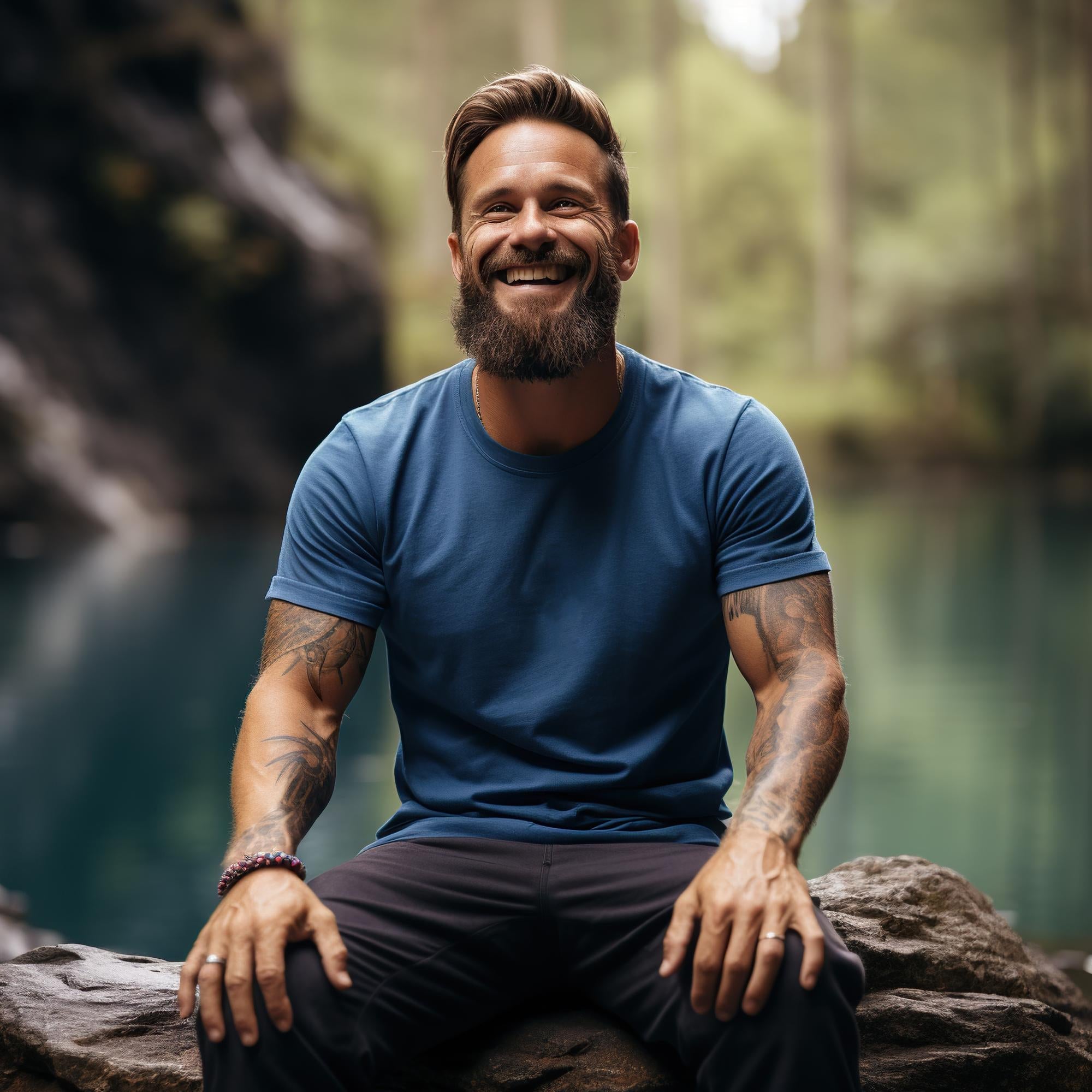 Smiling man in a blue shirt with a beard and tattoos is sitting outdoors, representing men's health and well-being.
