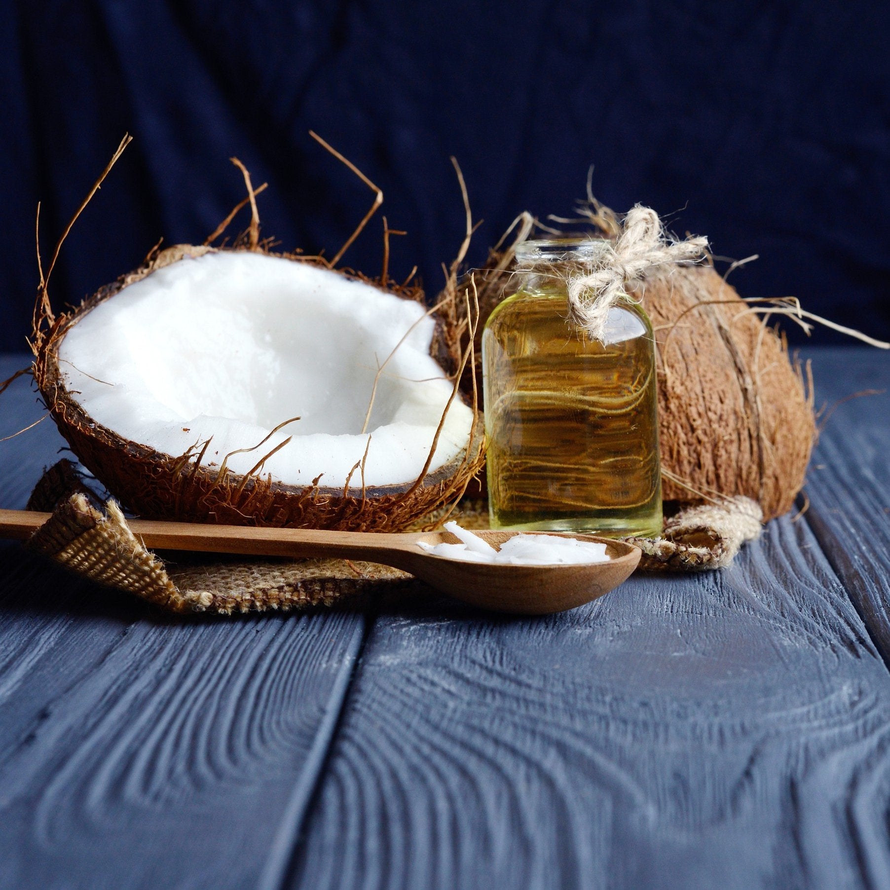 Halved coconut, whole coconut, oil jar, and wooden spoon on dark wood signify ketones for ketogenic diets, providing an alternative energy source.