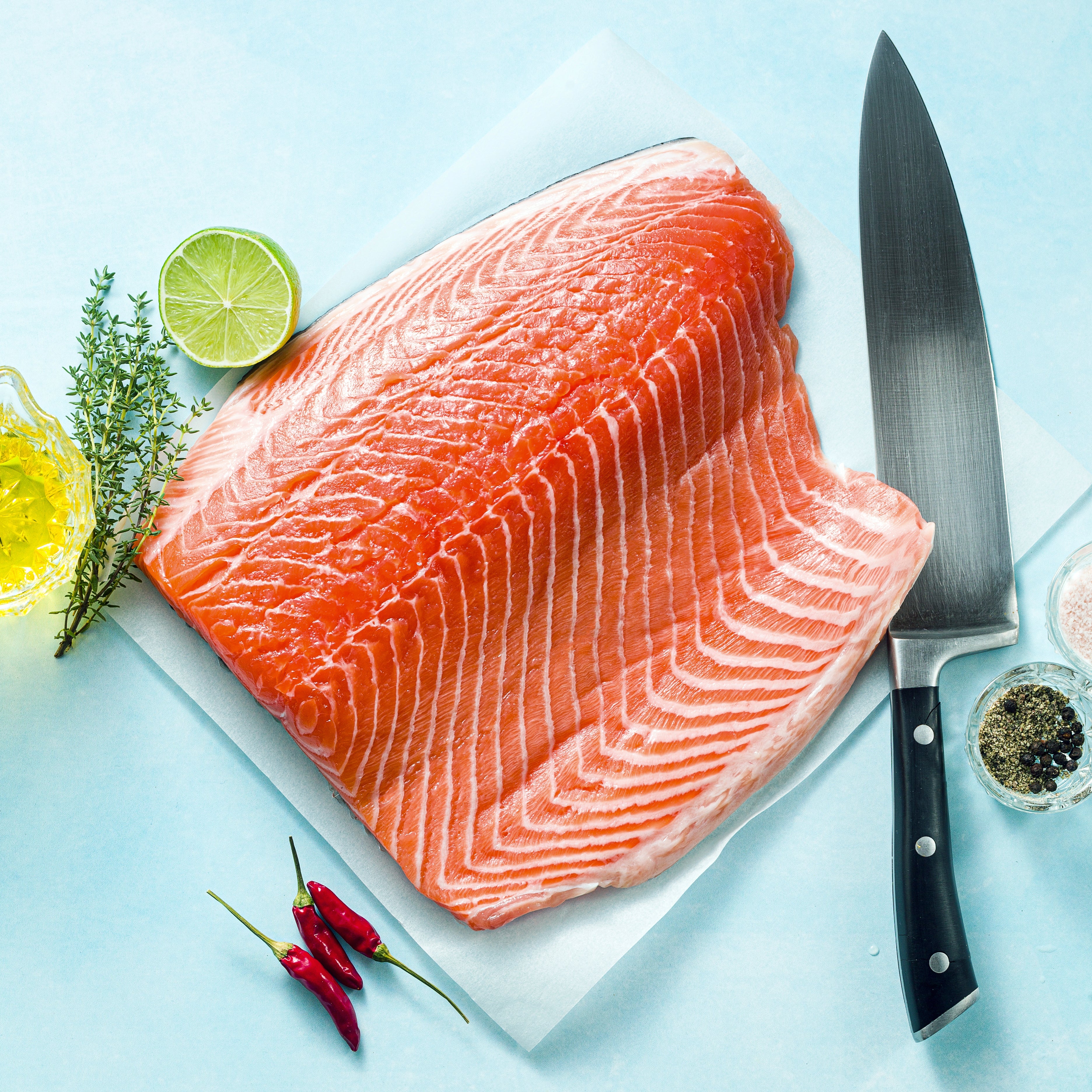 Fresh salmon fillet on parchment paper with lime, thyme, oil, and chili peppers emphasizes Omega Fatty Acids for heart support and maintaining overall health.