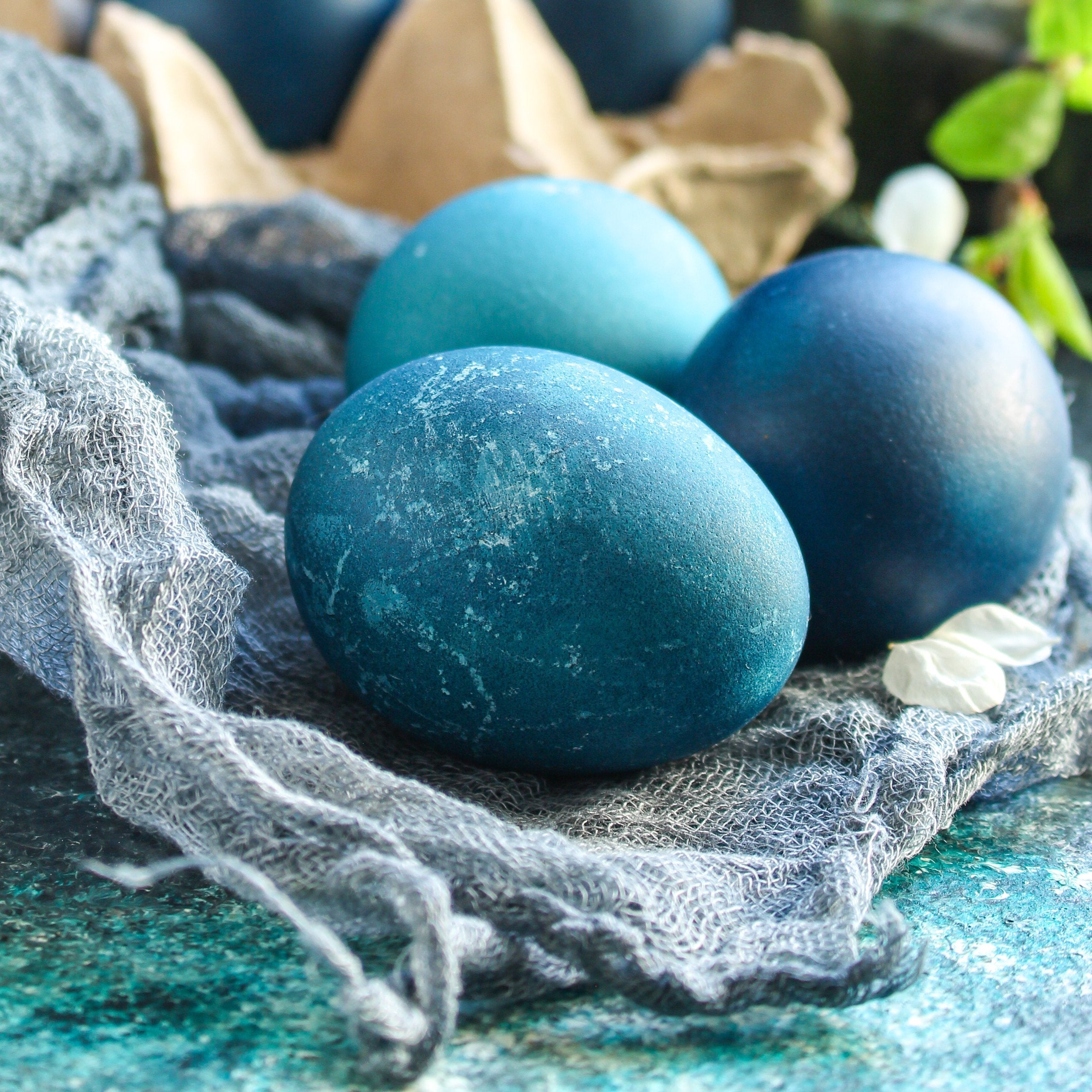 Three blue Easter eggs nestled beside white flowers on cloth; proteins for muscle building & repair lie within, promoting health with vital nutrients.