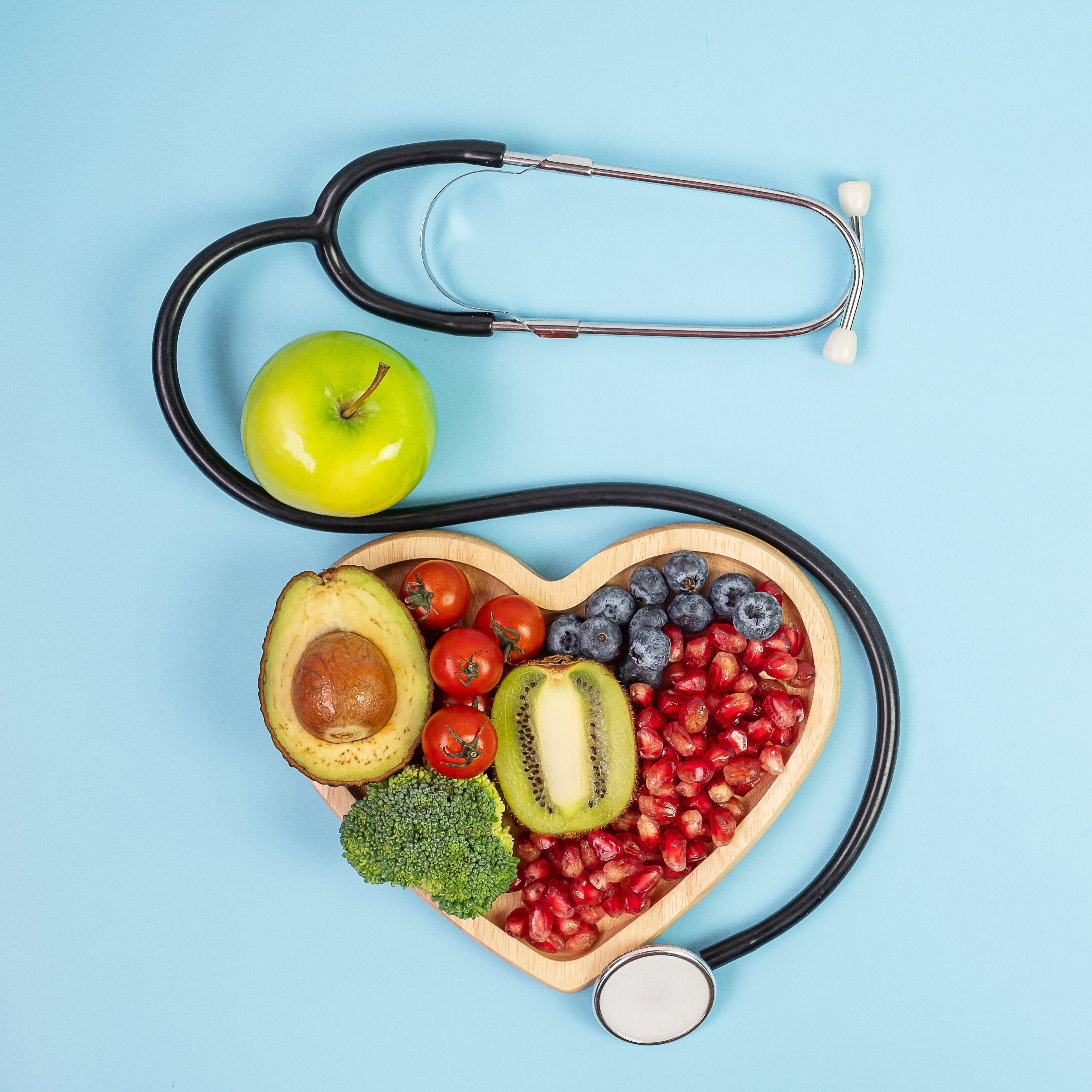 Stethoscope surrounds heart-shaped bowl of fruits and vegetables, promoting metabolic health and vitality for weight management.