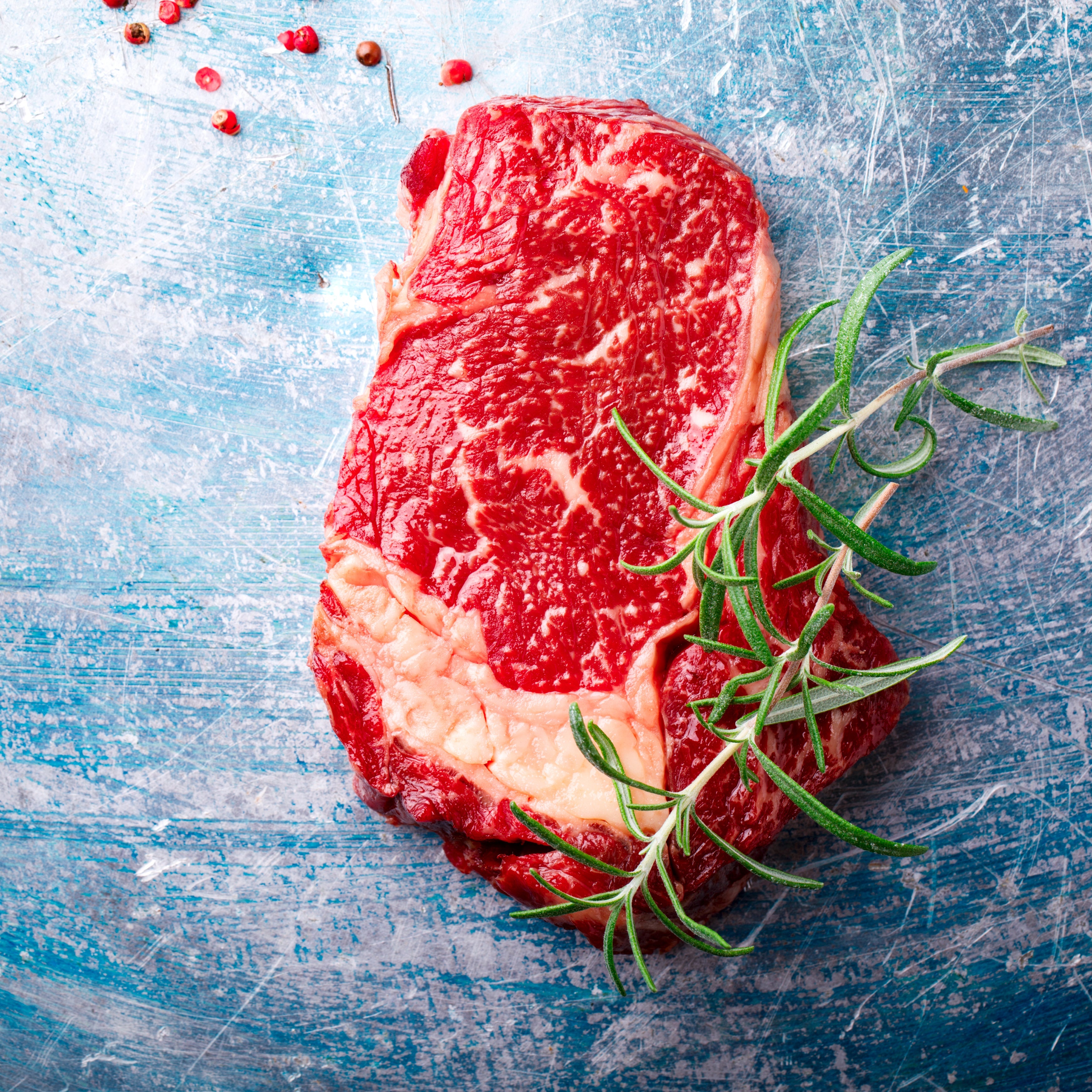 Raw steak garnished with rosemary and peppercorns on a blue surface rich in amino acids for metabolic health and bodily support.