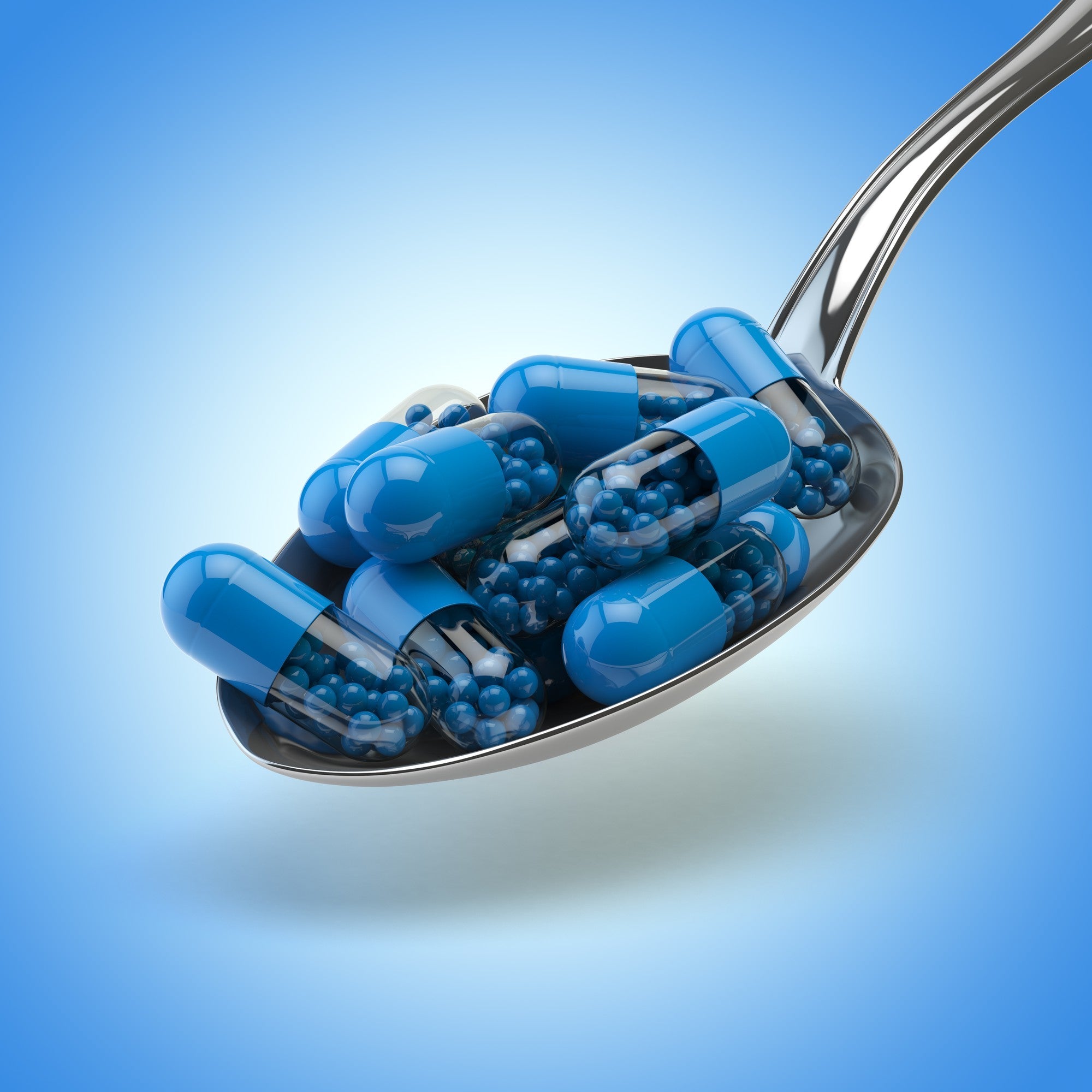 Metal spoon filled with various blue capsules, represents multivitamins and energy levels for a balanced well-being.